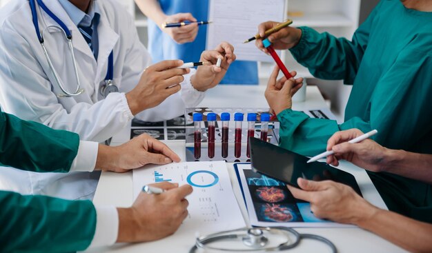 Equipe médica tendo uma reunião com médicos em casacos de laboratório brancos e roupas cirúrgicas sentados em uma mesa discutindo pacientes trabalhando on-line usando computadores