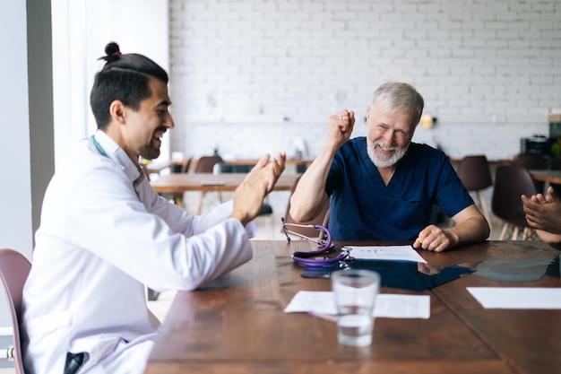 Equipe multiétnica amigável de médicos felicita o vencedor do líder médico masculino maduro feliz aplaude no escritório Colegas étnicos mistos alegres aplaudindo Conceito de medicina e cuidados de saúde