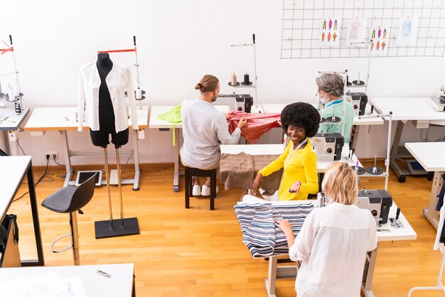 Equipe multiétnica de designers de moda trabalhando em uma oficina de criação de roupas - Grupo multirracial de estilistas, estilistas e costureiras trabalhando em uma nova coleção