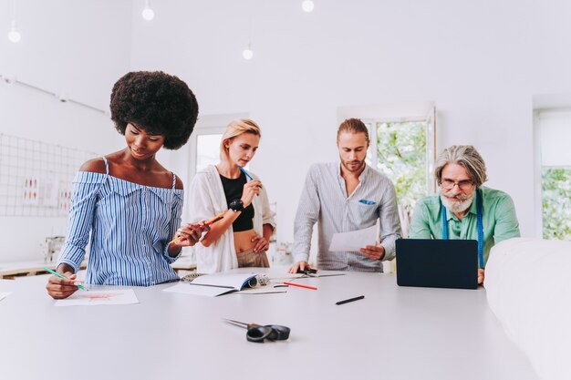 Equipe multiétnica de designers de moda trabalhando em uma oficina de criação de roupas - grupo multirracial de estilistas, estilistas e costureiras trabalhando em uma nova coleção