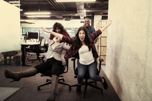 equipe multiétnica de empresa de startups de desenvolvedores de software se divertindo enquanto corria em cadeiras de escritório, funcionários diversos animados rindo desfrutando de atividades engraçadas no intervalo do trabalho, funcionários criativos e amigáveis.