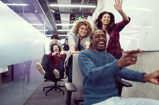 Foto equipe multiétnica de empresa de startups de desenvolvedores de software se divertindo enquanto corria em cadeiras de escritório, funcionários diversos animados rindo desfrutando de atividades engraçadas no intervalo do trabalho, funcionários criativos e amigáveis.