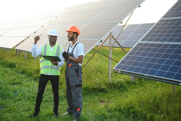 Equipe multirracial de engenheiros em painéis solares Engenheiro afro-americano e árabe trabalhando em fazenda de painéis solares