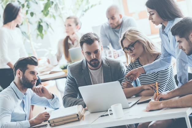 Equipe no trabalho. Grupo de jovens empresários trabalhando e se comunicando enquanto estão sentados na mesa do escritório, juntamente com colegas sentados ao fundo