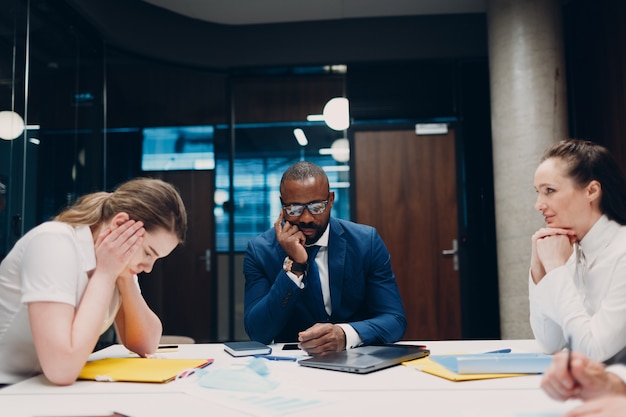 Equipe triste do empresário e da empresária na reunião do escritório. Pessoas de negócios agrupam a discussão da conferência com o chefe.