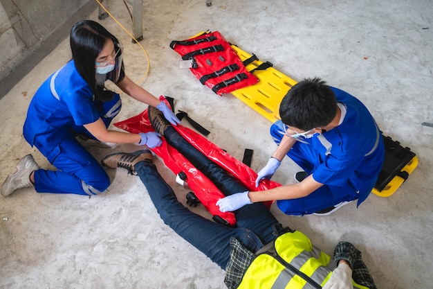 Equipes médicas de emergência estão ajudando um trabalhador da construção civil com um acidente na perna quebrada em um canteiro de obras. equipe de segurança ajuda acidente com funcionário.