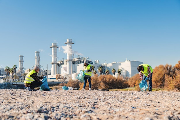 Equipo de activistas ambientales voluntarios recogiendo basura plástica de la arena en la playa cerca de una fábrica Grupo de personas limpiando la naturaleza para reciclar la basura Concepto ambientalista