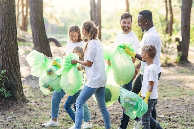 Equipo activo de amantes de la naturaleza internacionales en camisetas blancas que recogen basura en paquetes de plástico en el bosque.