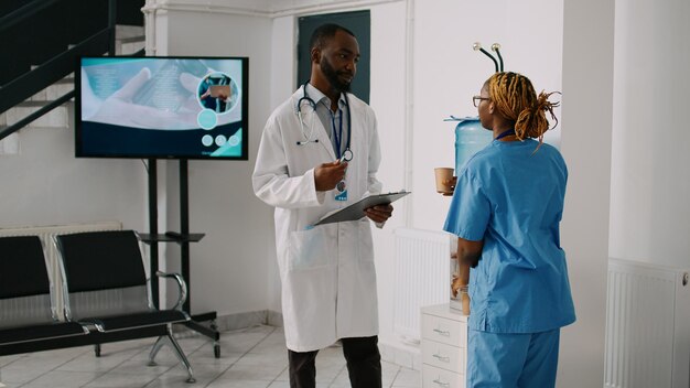 Equipo afroamericano de especialistas hablando de citas y tratamientos de enfermedades en el vestíbulo de recepción del hospital. Enfermera y médico que trabajan en el centro de salud y discuten sobre medicina.