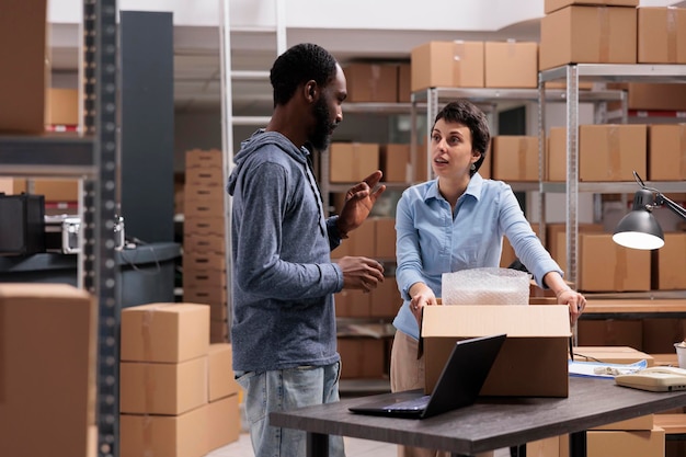 El equipo del almacén discute sobre la logística de distribución mientras coloca los productos del cliente en una caja de cartón después de envolver el pedido en una envoltura de burbujas. Empleado industrial trabajando con mercadería en almacén.