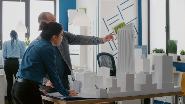 Equipo de arquitectos que planifican el diseño con planos y modelo de construcción en la mesa. Hombre y mujer trabajando juntos en el plan de distribución de la construcción, diseñando un proyecto de desarrollo urbano.