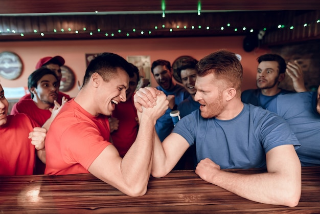 Foto equipo azul y rojo, los fanáticos de la lucha de brazos en el bar de deportes