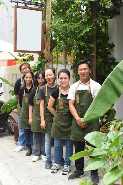 Equipo de cafetería vietnamita sonriendo y de pie juntos contra un café