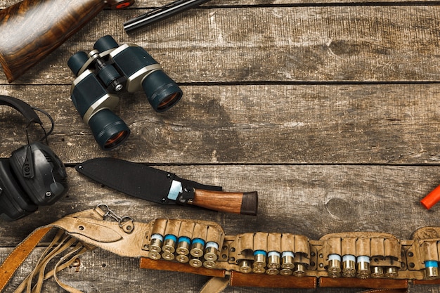 Equipo de caza sobre fondo de madera vieja, incluyendo binoculares y cartuchos de cuchillo de rifle