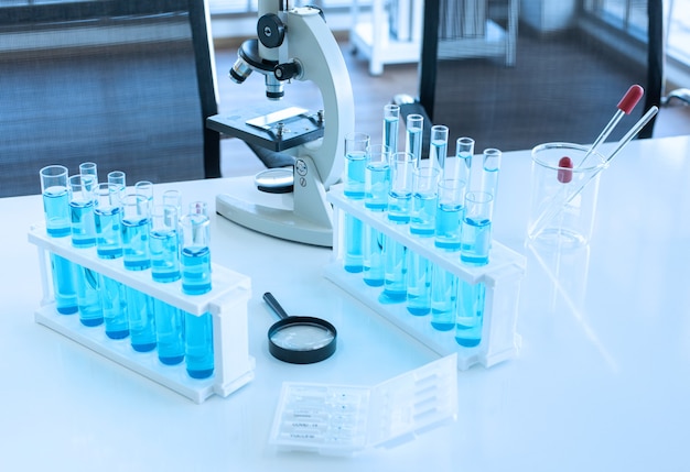 Equipo científico en la mesa de regazo como microscopio, vaso de precipitados, tubo de ensayo con líquido azul, pipeta y lupa