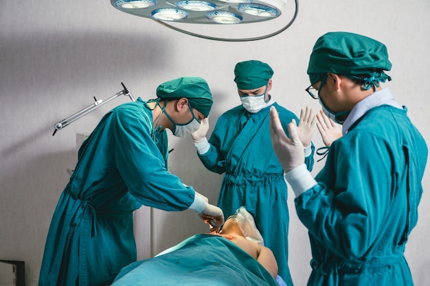 Equipo de cirujanos asiáticos en bata quirúrgica realizando cirugía a un paciente gravemente herido en quirófano en el hospital