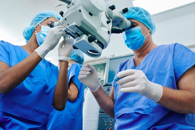 Equipo de cirujanos mirando a través de microscopio quirúrgico realizando corrección de la visión ocular con láser