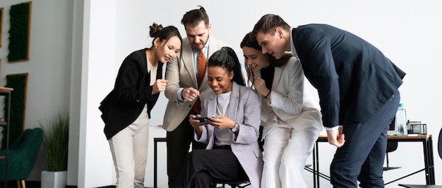 Un equipo de colegas en la oficina observa con interés cómo un empleado juega con un teléfono móvil