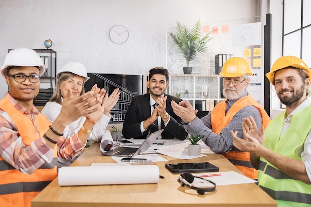 Foto equipo de construcción con trajes y cascos sentados a la mesa con planos y artilugios