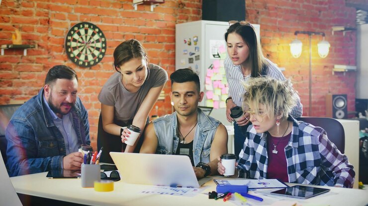 El equipo creativo del grupo con café para llevar discute ideas usando una computadora portátil en el estudio