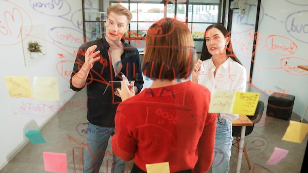 Equipo creativo de inicio de tormenta de ideas de marketing mientras una mujer de negocios caucásica cooperativa presenta una solución creativa frente a un tablero de vidrio en una reunión de negocios Trabajando juntos Inmaculada.