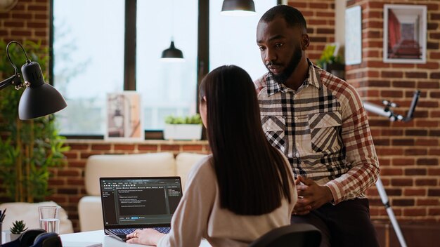 Equipo creativo interracial programando código en una computadora portátil y depurando