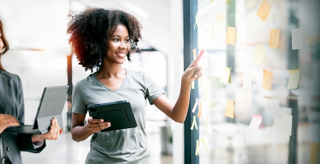 El equipo creativo de una joven empresaria usa notas post-it en una pared de vidrio para escribir un plan de negocios de estrategia para el crecimiento del desarrollo hasta el éxitox9