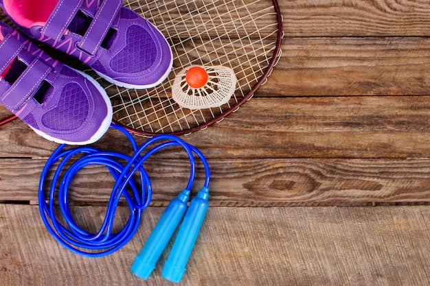 Equipo deportivo: el pajarito está en la raqueta, saltando la cuerda, nadando gafas y zapatillas de deporte en el fondo de madera