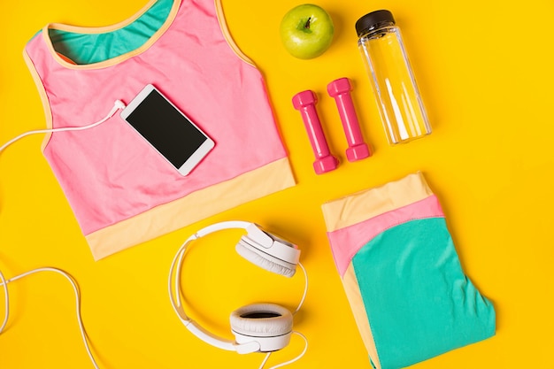 Foto equipo deportivo y ropa con teléfono móvil en la vista superior de fondo amarillo