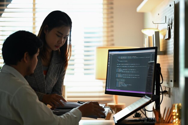 Equipo de desarrolladores de software trabajando con datos codificados en la pantalla de la computadora en una habitación oscura