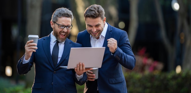 Equipo de dos hombres de negocios emocionados usando una computadora portátil al aire libre hombres de negocios que buscan una computadora portátil con su negocio su