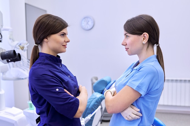 Equipo de dos médicos mujeres dentistas en el consultorio dental, colegas mujeres miran, ver de perfil. Concepto de medicina, odontología y salud.