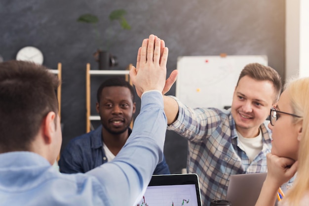 Equipo empresarial hablando de los resultados de su trabajo. Grupo de empresarios alegres discutiendo una estrategia de marketing exitosa, dos hombres dando cinco, espacio de copia