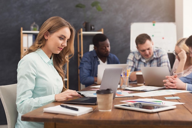 Equipo empresarial hablando de los resultados de su trabajo. Grupo de empresarios alegres discutiendo la nueva estrategia de marketing, mujer joven escribiendo en la computadora portátil, espacio de copia