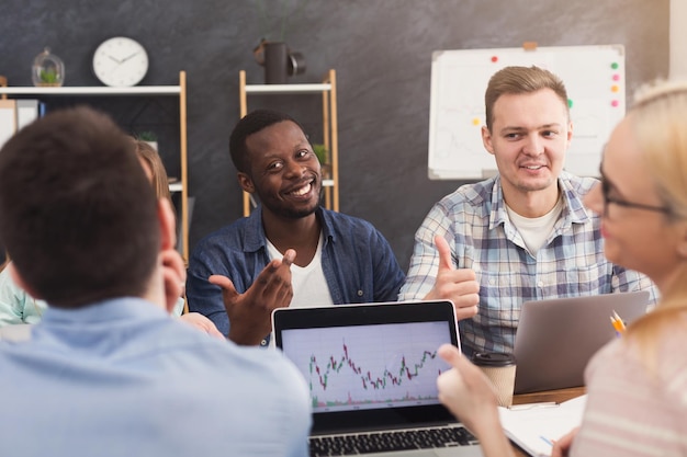 Equipo empresarial hablando de los resultados de su trabajo. Grupo de empresarios alegres que estudian el gráfico en la computadora portátil, discutiendo la nueva estrategia de marketing, sentados en la oficina, espacio de copia