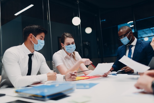 Equipo de empresario y empresaria en mascarilla médica en la reunión de la oficina. Discusión de la conferencia del grupo de personas de negocios con el jefe.