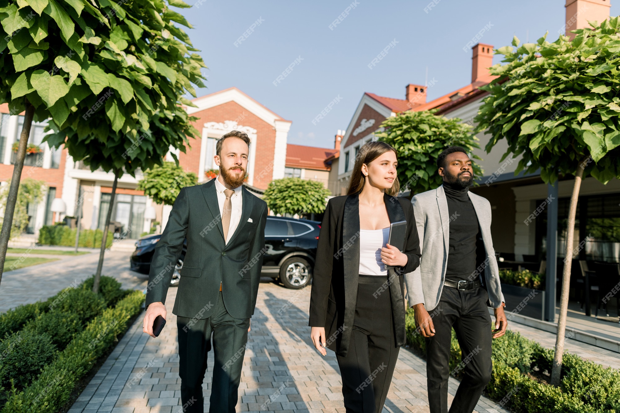 Equipo de empresarios multiétnicos hombres y en ropa casual elegante, caminando al aire libre en la de negocios. mujer tiene tableta digital. coche negro y edificios modernos. | Foto