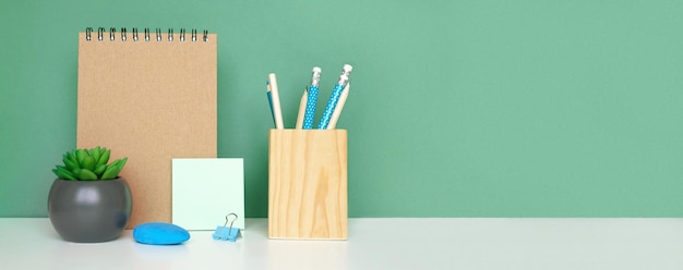 Equipo escolar sobre fondo de pared verde de mesa blanca Educación Suministros de madera Escritorio de regreso a la escuela