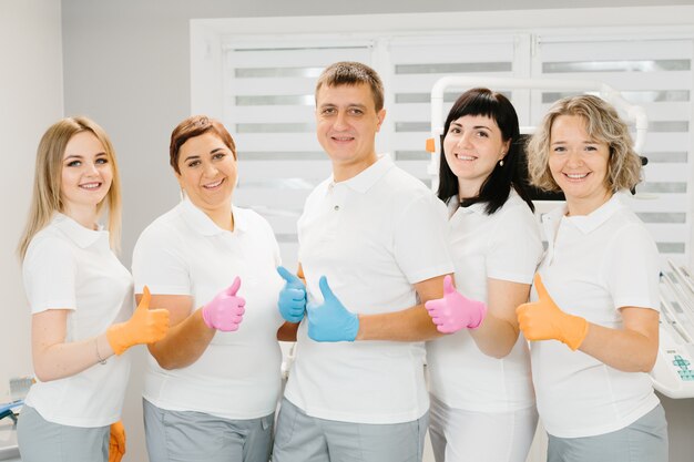 Equipo feliz en el dentista levantando sus pulgares en guantes de color