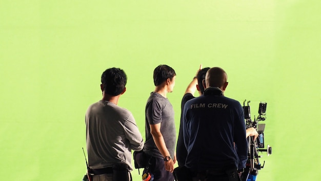 Equipo de fotógrafos y equipo de filmación y cámara de video en línea de alta definición y fondo de pantalla verde para filmar películas en un gran estudio.