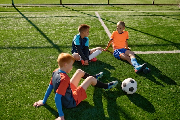 Equipo de fútbol de adolescentes hablando en el campo de fútbol descansando después del entrenamiento o del partido