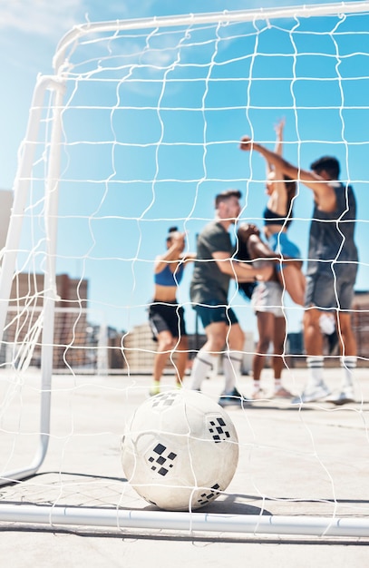 Foto equipo de fútbol y pelota en el poste de la portería o en la red con un grupo de deportes de diversidad de hombres y mujeres en celebración de ganar y anotar en la azotea urbana ejercer entrenamiento y campeones concretos