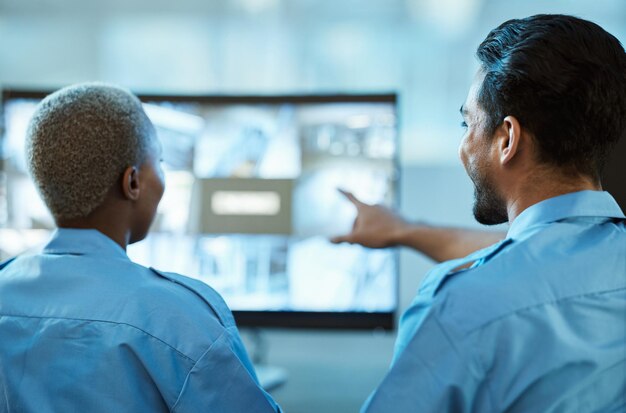 Equipo de guardia de seguridad y sala de control con una pantalla de computadora para la vigilancia Detrás de una mujer y un hombre apuntando al monitor de CCTV para la supervisión y monitoreo de la investigación de delitos cámara en vivo