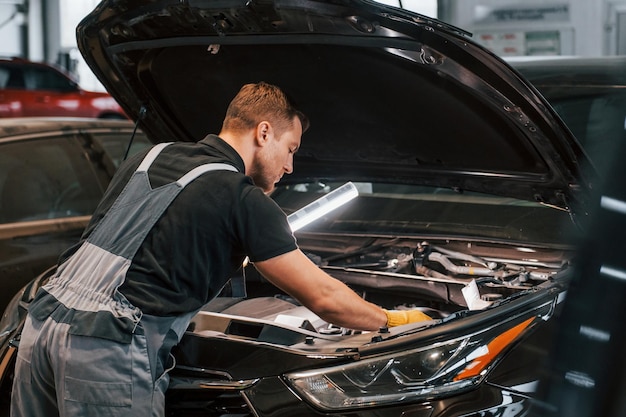 Con equipo de iluminación El hombre uniformado está trabajando en el servicio de automóviles