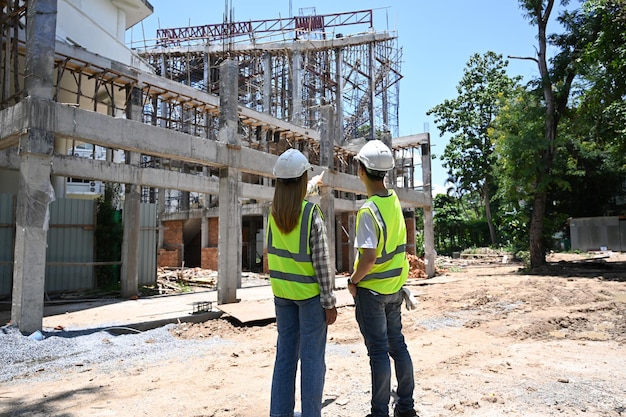 El equipo de ingenieros civiles de vista trasera con chalecos amarillos está discutiendo el proceso de construcción juntos en el sitio de construcción