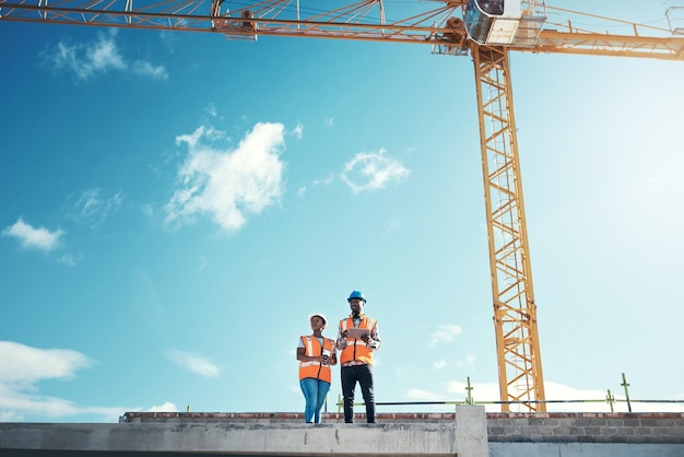 Equipo de ingenieros de techos del edificio hablando en el sitio de construcción al aire libre para el desarrollo de la visión o la arquitectura Mujer y hombre negros para la planificación del trabajo en equipo de ingeniería o discusión de seguridad con la maqueta del cielo