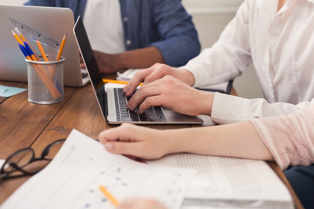 Equipo irreconocible de jóvenes empresarios que trabajan en la computadora portátil, escribiendo en la computadora, espacio de copia