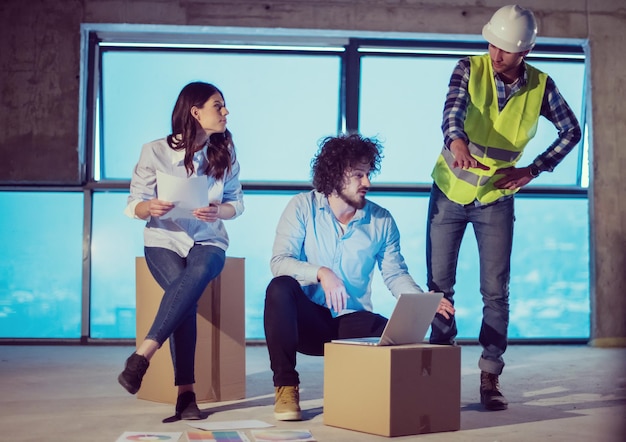 equipo joven de empresarios en grupo, arquitecto e ingeniero en el sitio de construcción revisando documentos y flujo de trabajo de negocios usando una computadora portátil en una nueva oficina de inicio