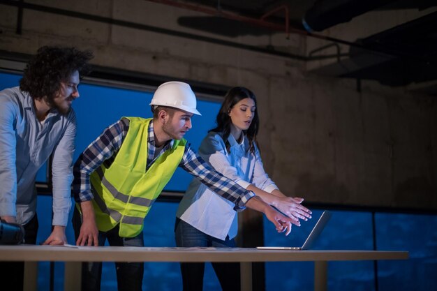 equipo joven de empresarios en grupo, arquitecto e ingeniero en el sitio de construcción revisando documentos y flujo de trabajo de negocios usando una computadora portátil en una nueva oficina de inicio