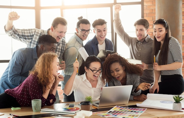 El equipo de jóvenes diseñadores disfruta del éxito, mira la pantalla de la computadora, celebra el proyecto exitoso, negocia el contrato, gana la licitación, copia el espacio